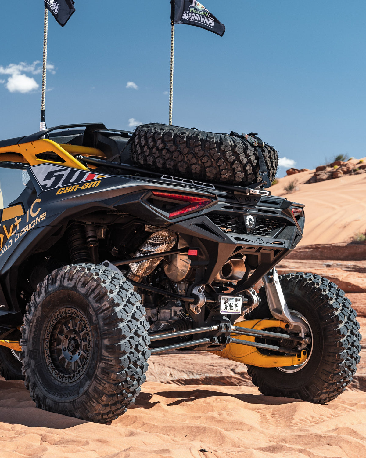 Rear Volt Bumper mounted on Can-Am Maverick R 2-Door viewed from driver's side rear quarter angle in a desert dune setting with hammer black powder coat finish