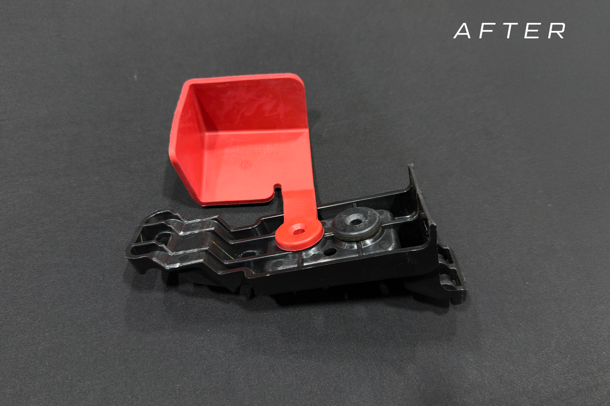 Black plastic automotive bracket with a red hinged cover
