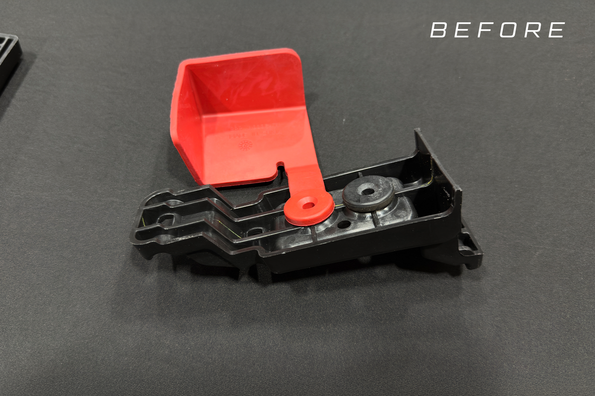 Black plastic automotive bracket with attached red protective cover