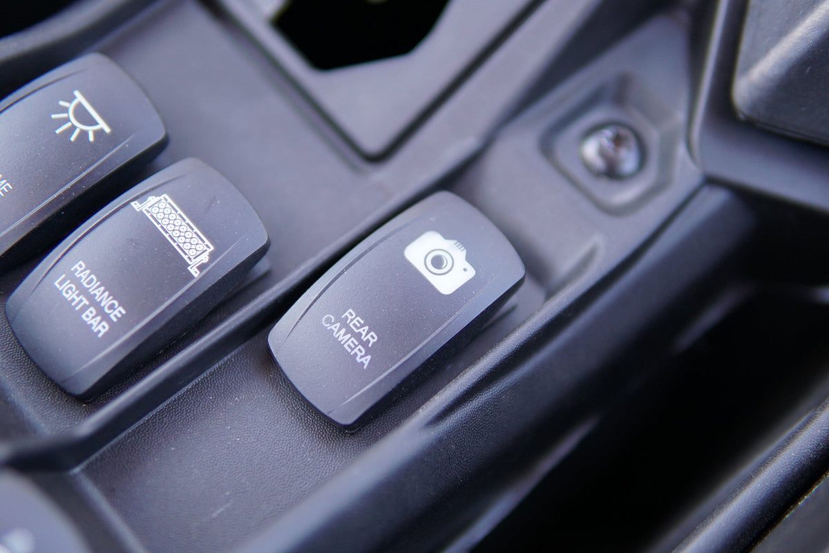 Dashboard rocker switch labeled rear camera with a camera icon