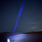 Blue laser pointer beam against a night sky with trees