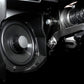 Close up of a circular vehicle speaker mounted in a black plastic housing next to metal mechanical components