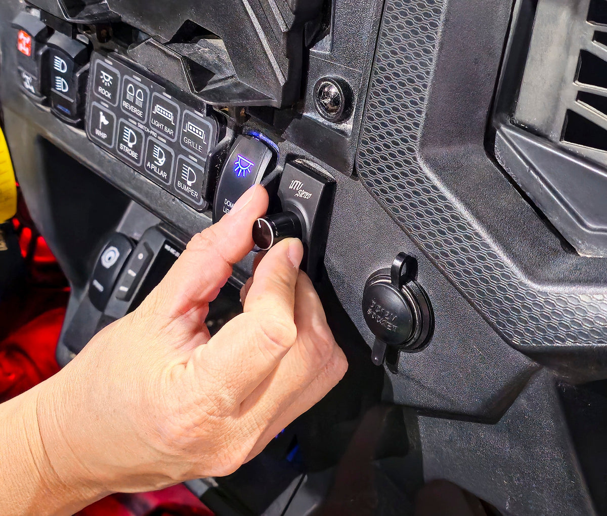 Hand adjusting a UTV Stereo volume knob mounted on a vehicle dashboard