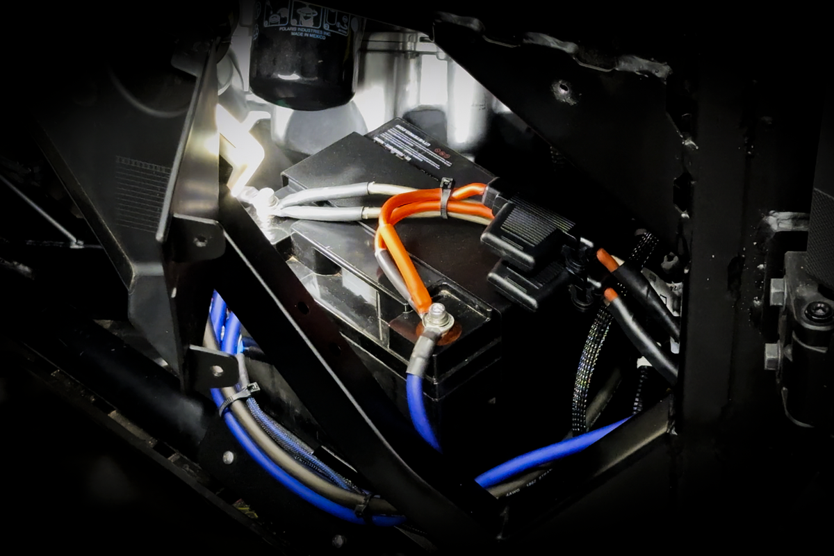 Vehicle battery with orange and blue wiring connections installed in engine bay