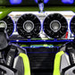 Four circular UTV Stereo speakers mounted on a green roll cage behind black bucket seats